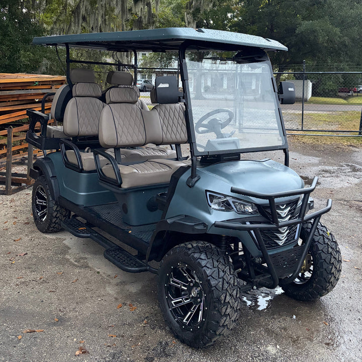 Golf cart with large off-road tires on a paved surface with trees in the background