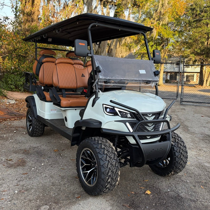 White golf cart with brown seats parked on a paved surface with trees in the background